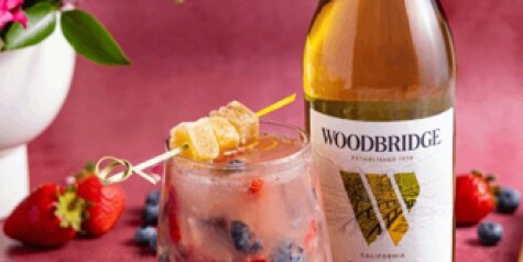A bottle of Woodbridge Chardonnay next to Woodbridge Ginger Smash, garnished with strawberries, blueberries and ginger candy.