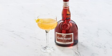 A yellow-colored Grand Marnier Spritz on a white marble tabletop, accompanied by a bottle of Grand Marnier Cordon Rouge.