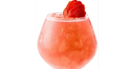 An ice-filled, clear wine glass holds a Strawberry Agave Spritzer cocktail garnished with a sliced strawberry.