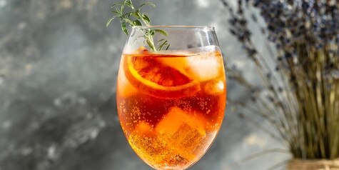 Citrus Spark cocktail with bloody oranges, sparkling wine and rosemary sprig in an ice-filled wineglass next to ingredients.