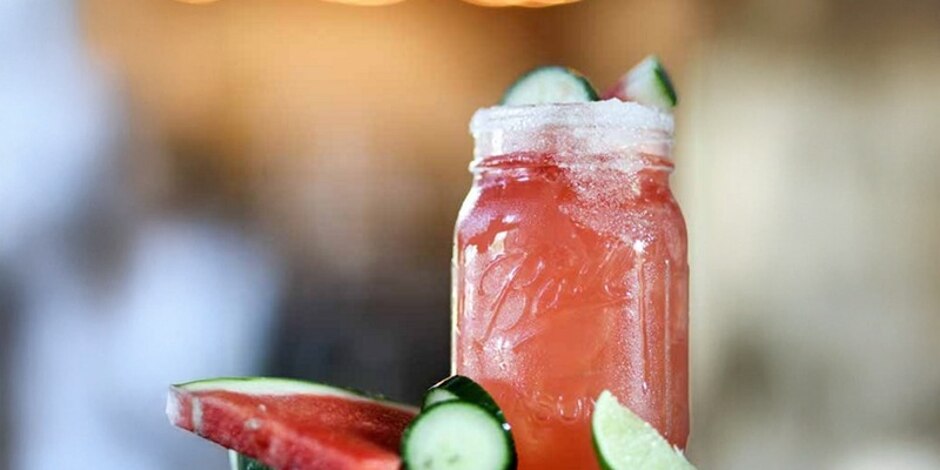 A Mason jar filled with The Firecracker cocktail is pictured near slices of cucumbers and watermelon.