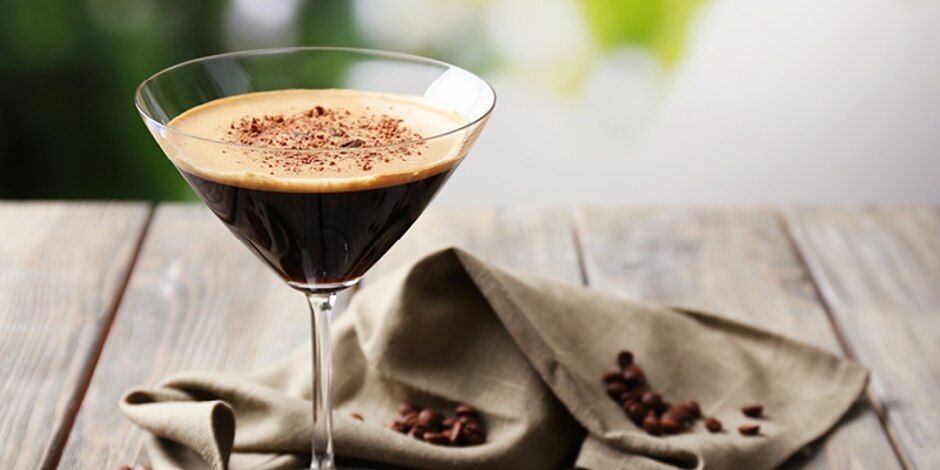 Espresso martini topped with ground cinnamon and coffee beans, on a picnic table with a dishtowel and coffee beans.