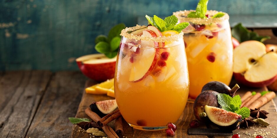 Two wineglasses rimmed with cinnamon sugar, filled with a white rum sangria and garnished with apples, figs and mint.