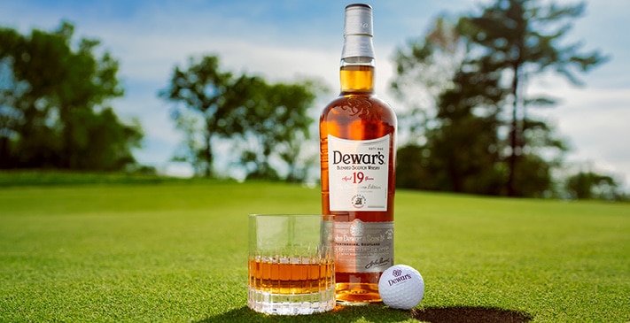 A green Elderflower Highball, surrounded by a golf ball, tees and bottles of Dewar’s Blended Scotch and Elderflower Liqueur.