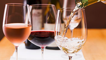 A glass of rosé, red wines next to a glass of white wine being poured.